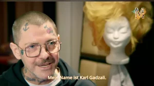 Der Wig-Designer Karl Gadzali neben einem Perückenkopf